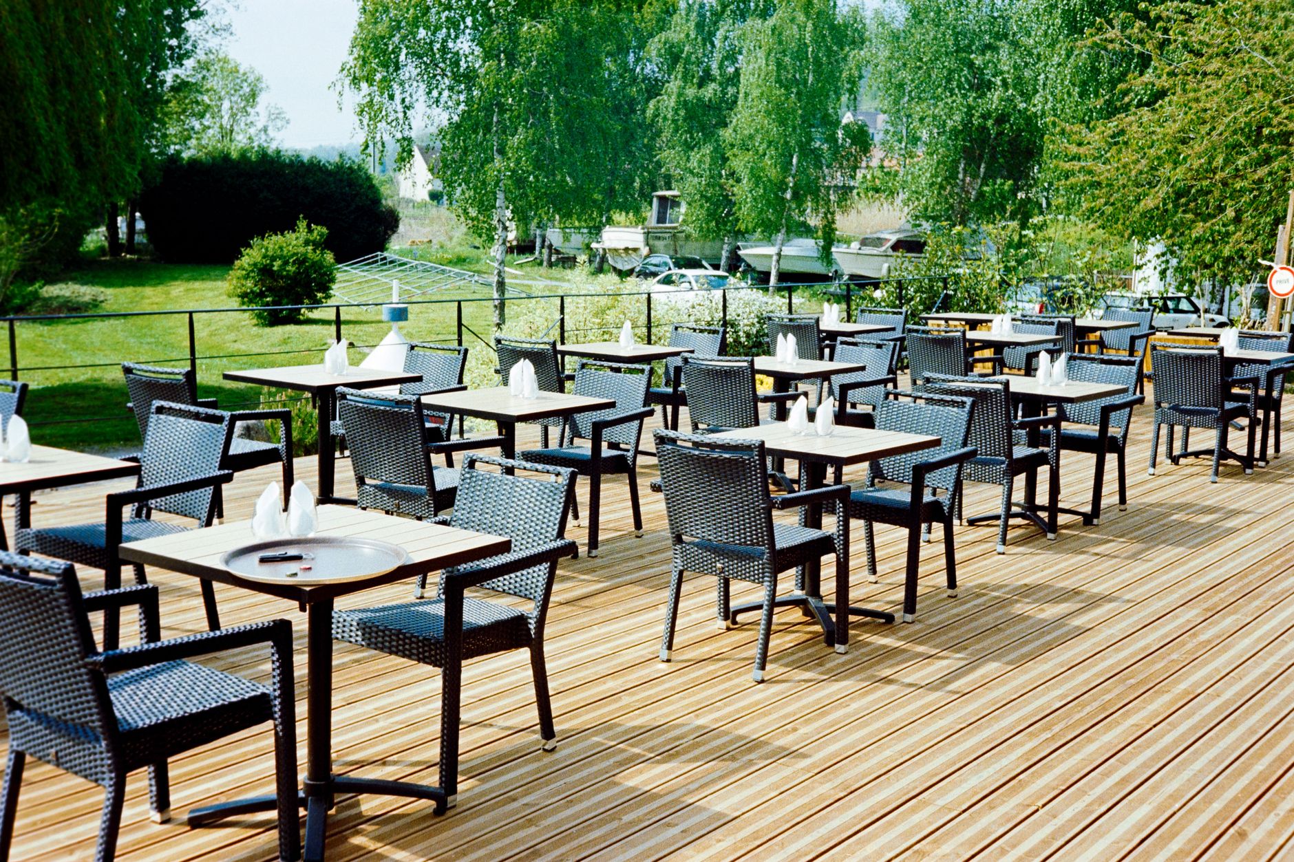 Friedlicher Blick auf eine leere Caféterrasse im Freien in Hauts-de-France, Frankreich, mit Korbmöbeln und üppigem Grün.