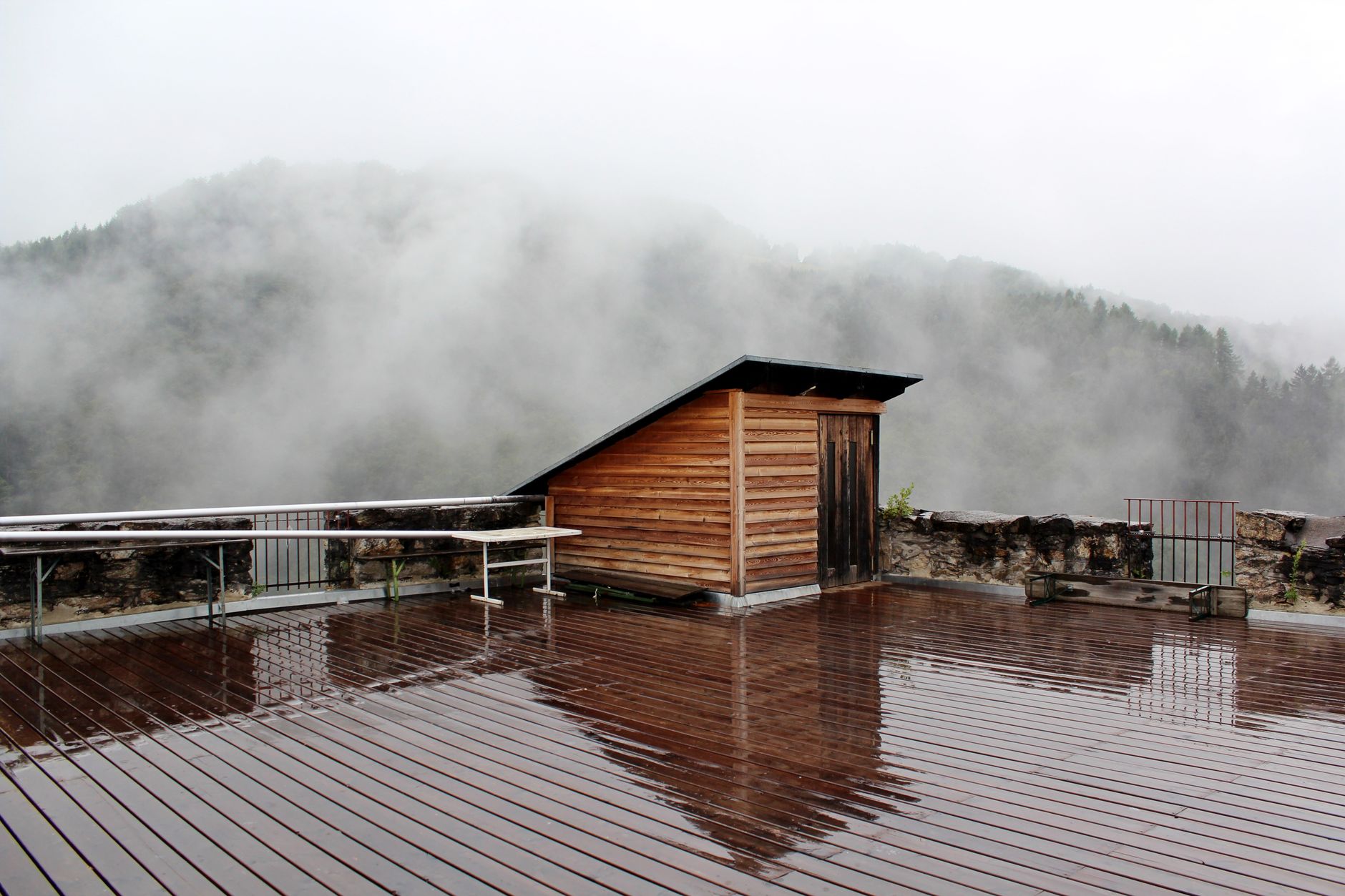 Ein ruhiger, nebliger Waldblick von einer regennassen Holzterrasse in Deutschlandsberg, Österreich.