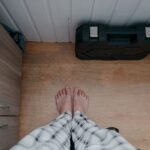 Draufsicht auf nackte Füße in Pyjamas auf einem Holzboden in einem Innenraum, daneben ein Werkzeugkasten.